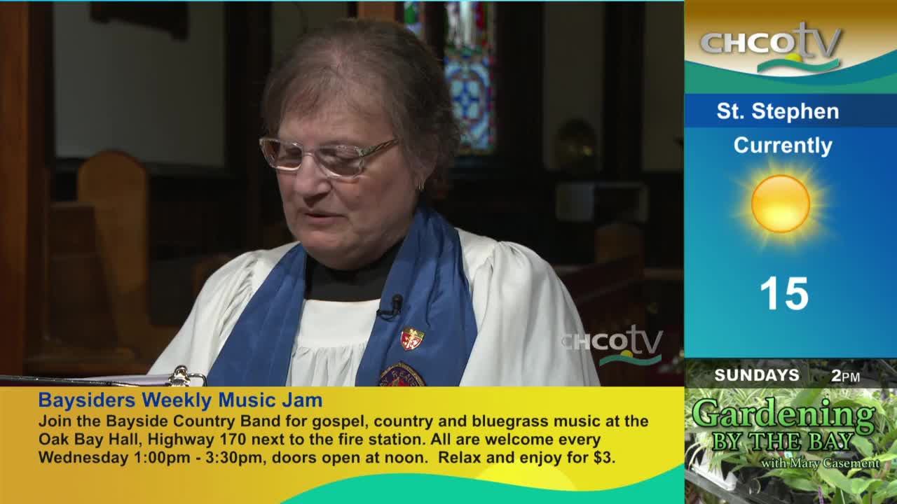 A woman in a blue stole and glasses is speaking, possibly reading, in front of a dark wooden backdrop. The CHCO-TV logo is visible, with a weather report for St. Stephen and a listing for "Baysiders Weekly Music Jam" at the bottom of the screen.
