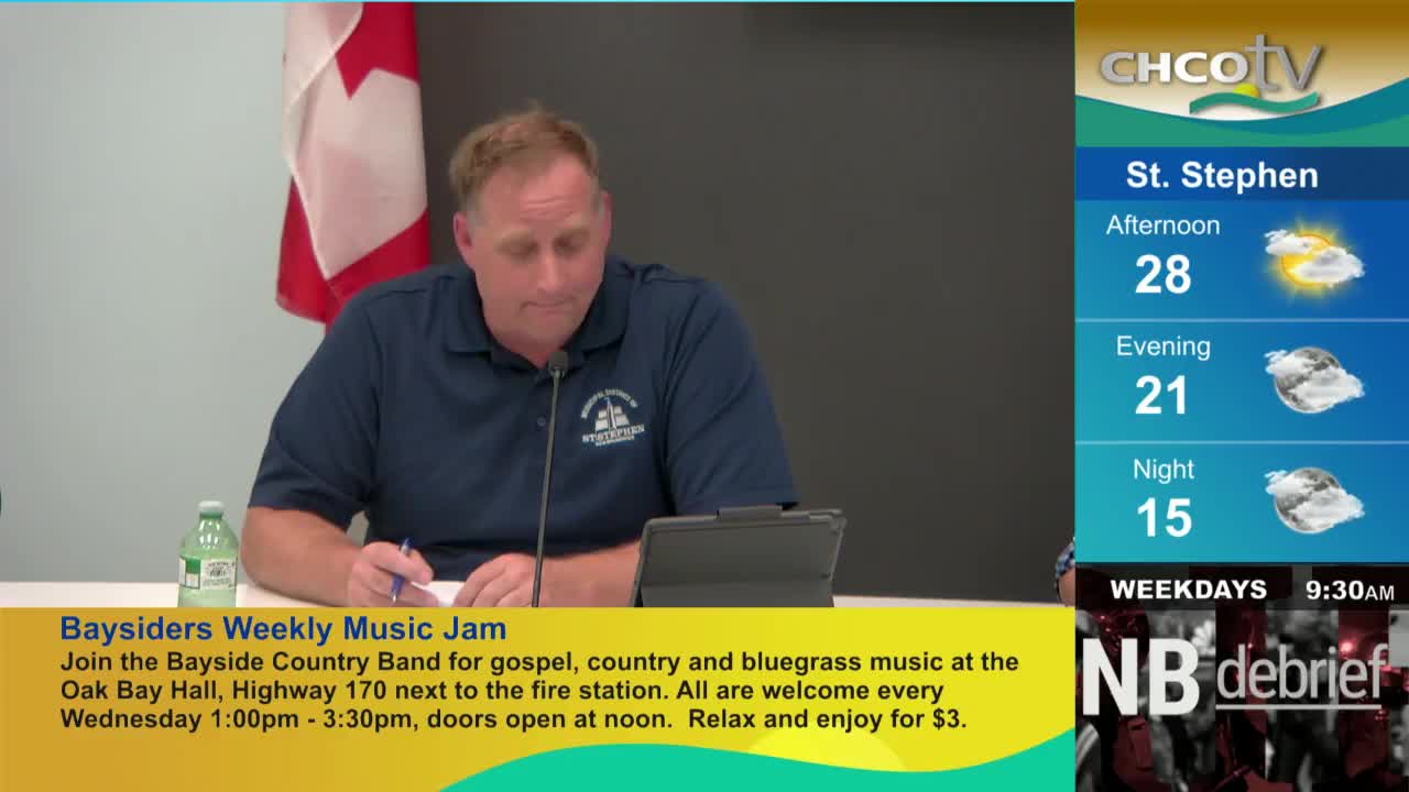 A man in a blue shirt is seated at a table, writing on a pad, with a Canadian flag in the background. CHCO-TV's weather forecast for St. Stephen is displayed on the right.
