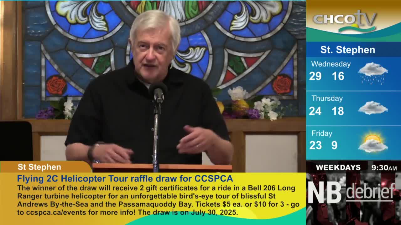 A man in a black shirt stands at a microphone, gesturing with his hands as he speaks. The CHCO-TV weather report for St. Stephen is displayed beside him.
