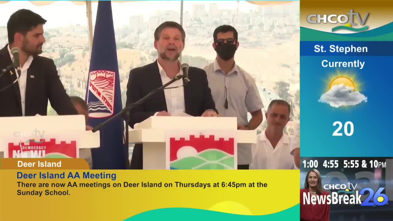A man in a suit speaks into a microphone at a podium, with two other men standing nearby. The CHCO-TV weather report in the corner shows a temperature of 20 degrees.
