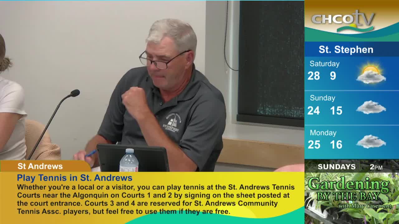 A man in a gray shirt, wearing glasses, sits at a table, looking down at a laptop. The CHCO-TV weather forecast for St. Stephen, Canada, is visible on the right side of the screen.
