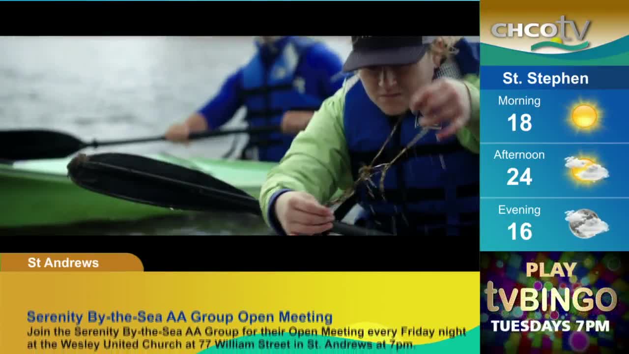 A person in a green jacket and a blue life vest is fiddling with something small in their hands. Another person paddles in the background, both of them in kayaks on the water, as seen on CHCO-TV.
