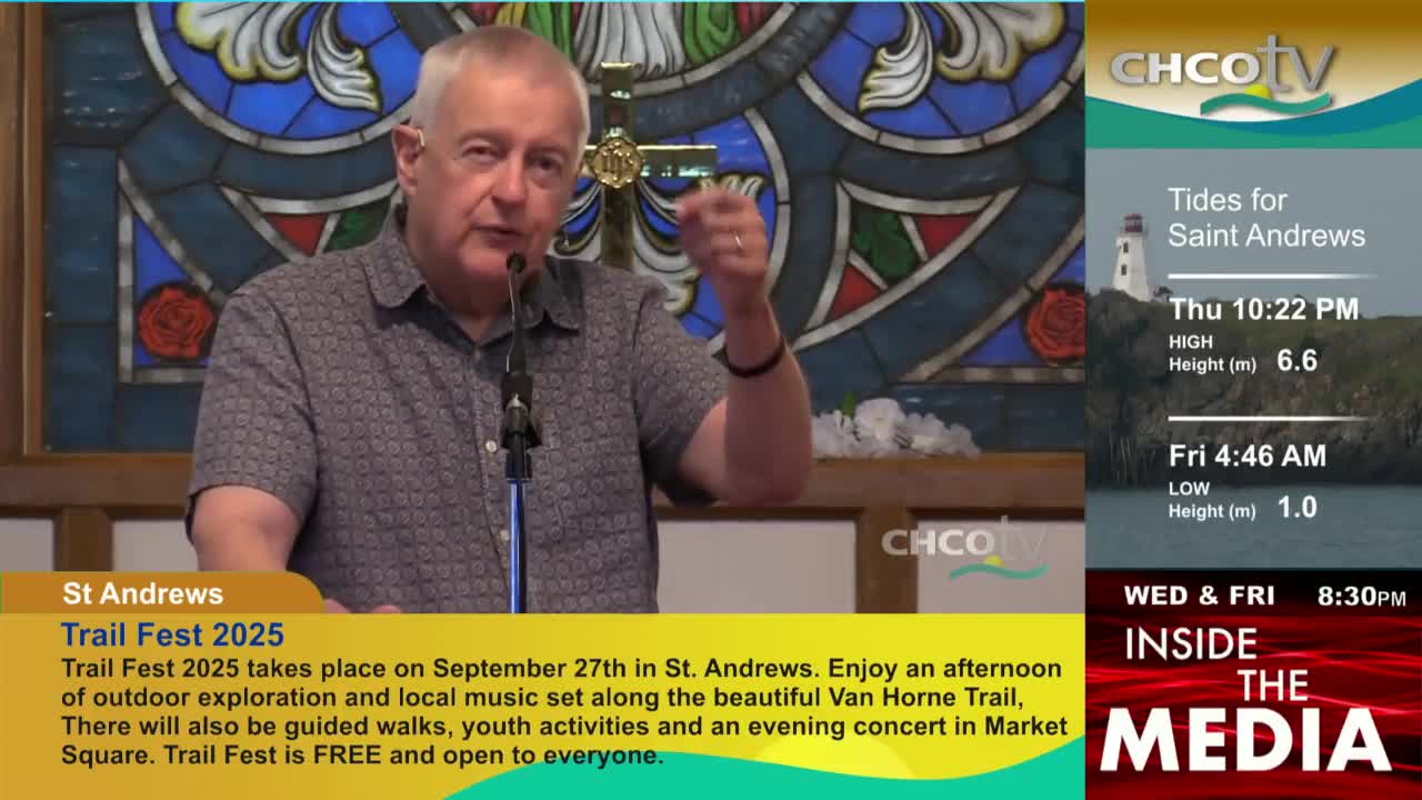 A man with gray hair gestures with his right hand, speaking into a microphone. The CHCO-TV logo is visible, along with information about tides and an upcoming event in St. Andrews, Canada.
