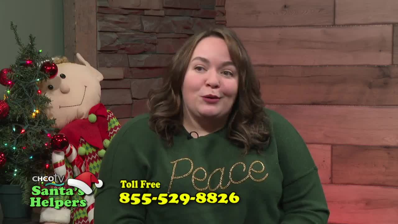 The woman in the green sweater speaks directly to the camera, a "Peace" design glittering on her chest. Behind her, a Christmas tree and a large elf doll stand beside the CHCO-TV Santa's Helpers logo.
