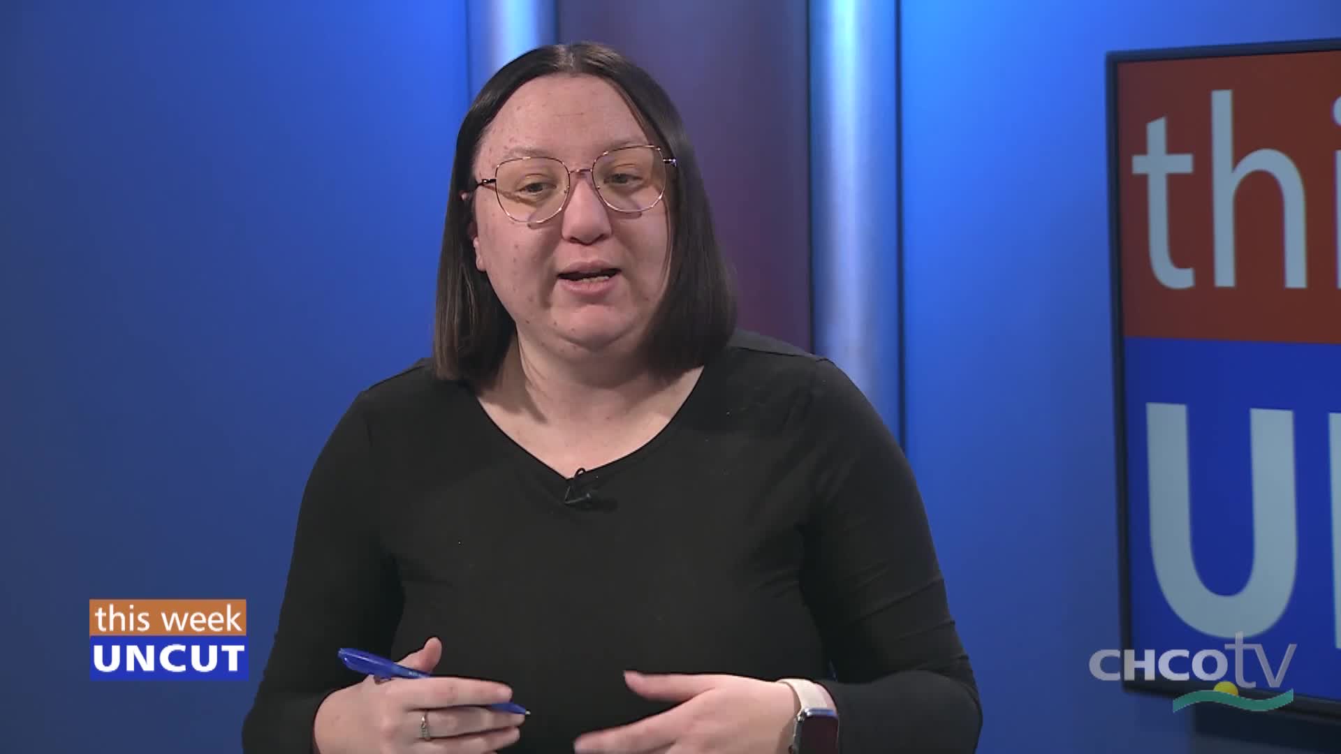 A woman in a black shirt gestures with a blue pen while speaking. Behind her, a screen displays "this week UNCUT" and the CHCOtv logo.