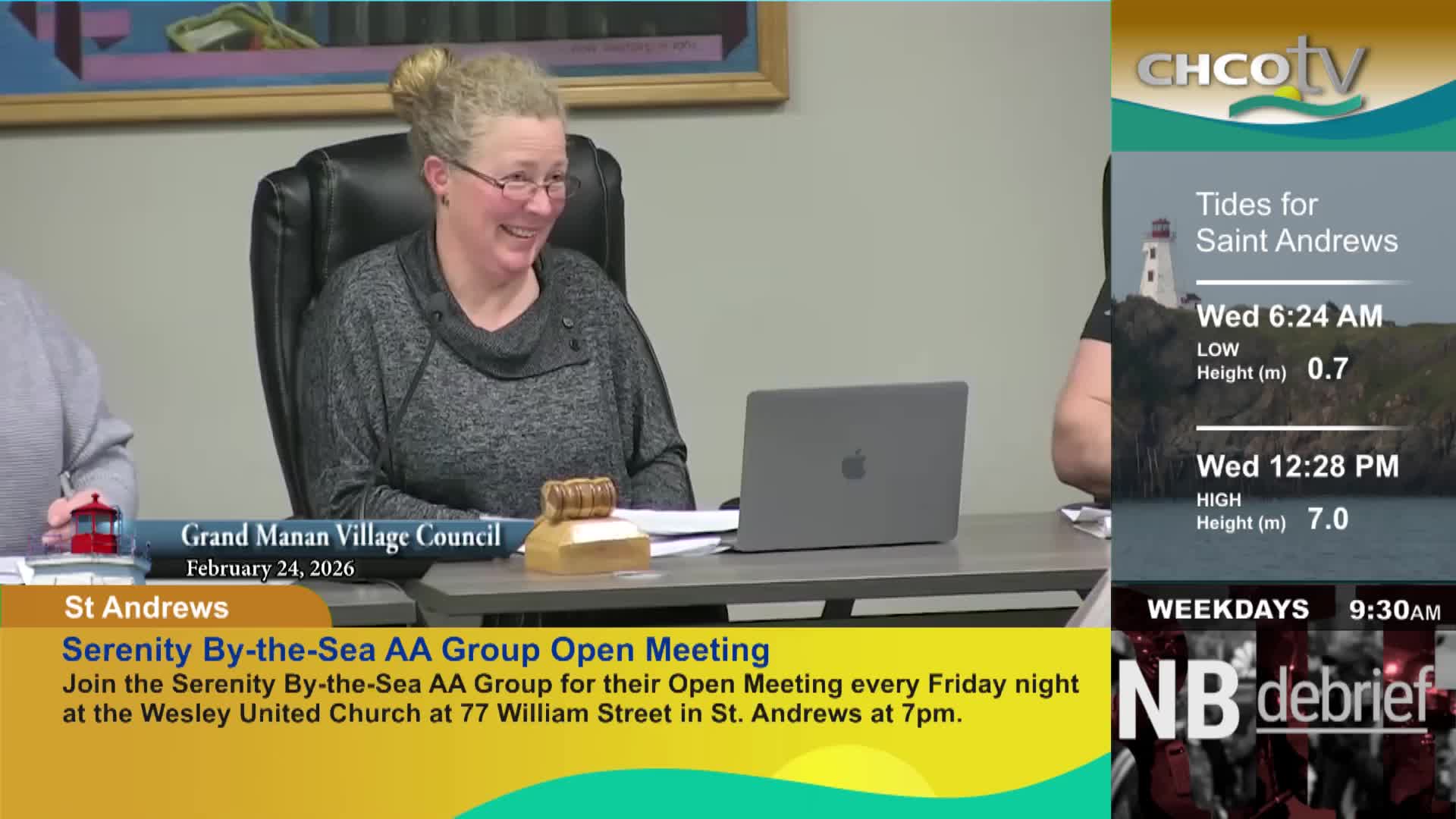 A woman with her hair pulled back laughs while sitting at a table in front of a laptop. A CHCO-TV graphic displays tide information for Saint Andrews beside her.