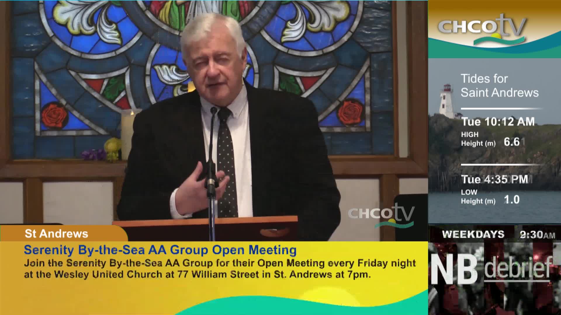 A man in a suit speaks at a podium, his right hand gesturing. On the right, CHCO-TV displays tide information for Saint Andrews and a local news program.