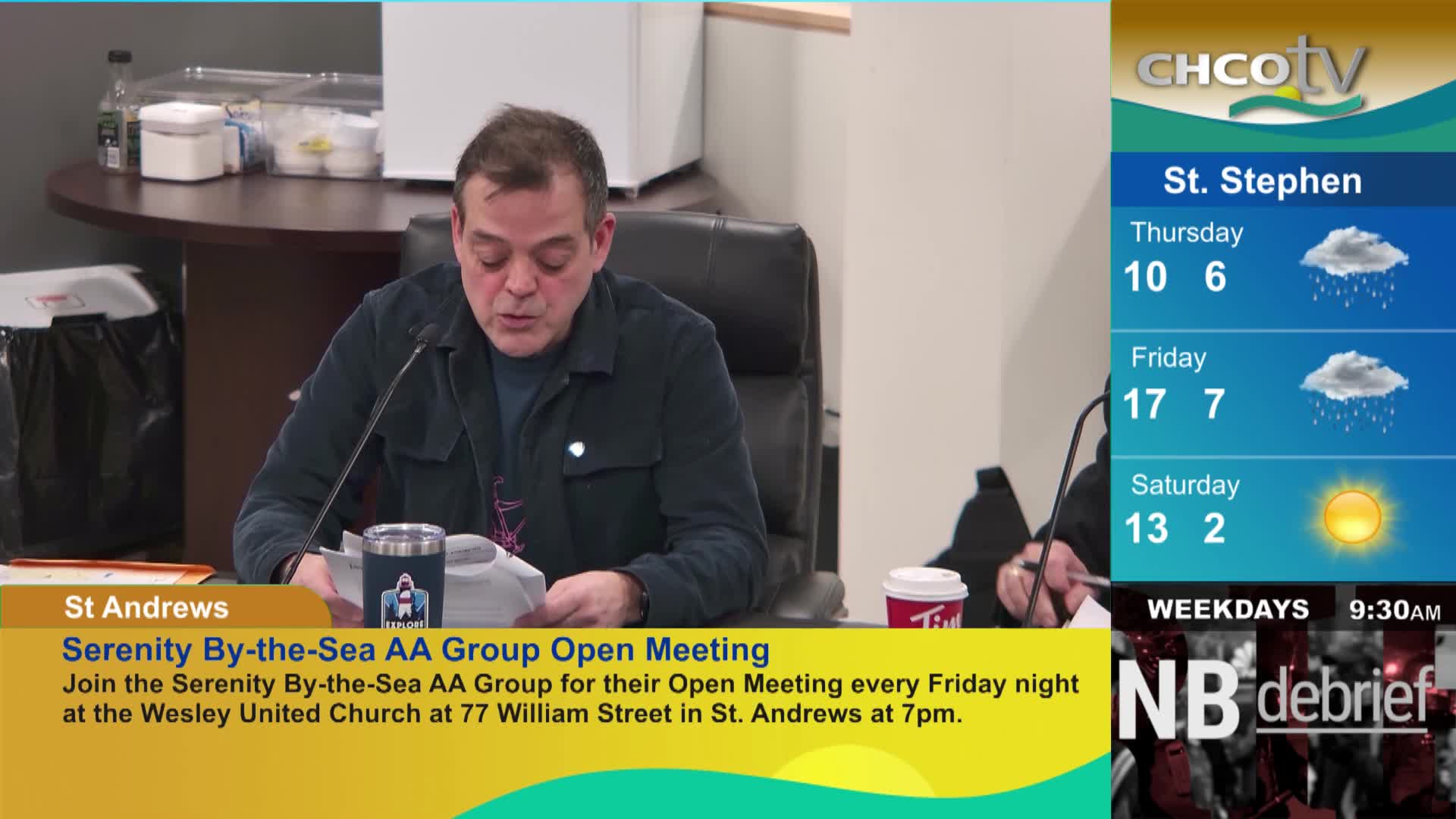A man reads from papers at a table, a CHCO-TV weather report for St. Stephen displayed to his right. The report shows rain for Thursday and Friday, with sun on Saturday.