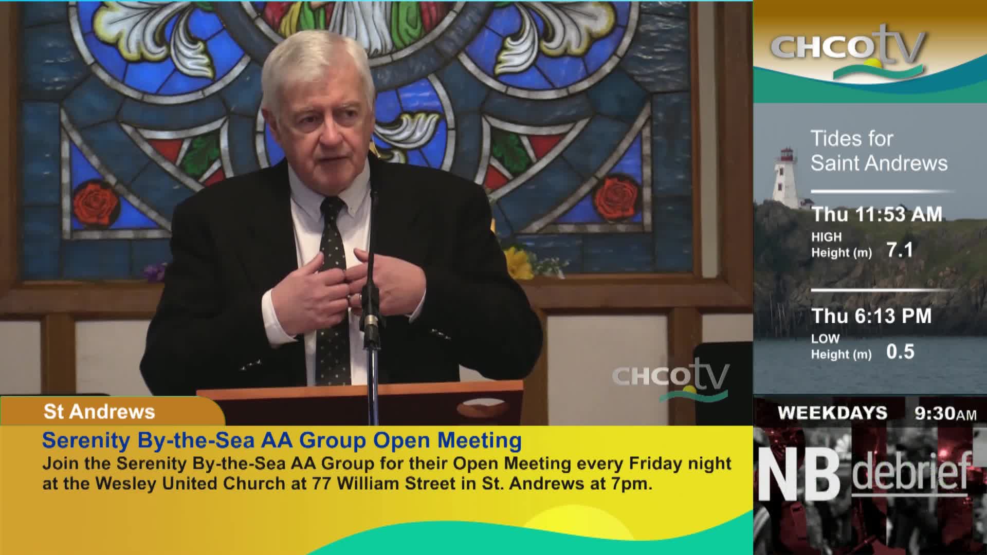 A man in a suit speaks at a podium, his hands gesturing as he talks. On the right, CHCO-TV displays tide information for Saint Andrews, New Brunswick.