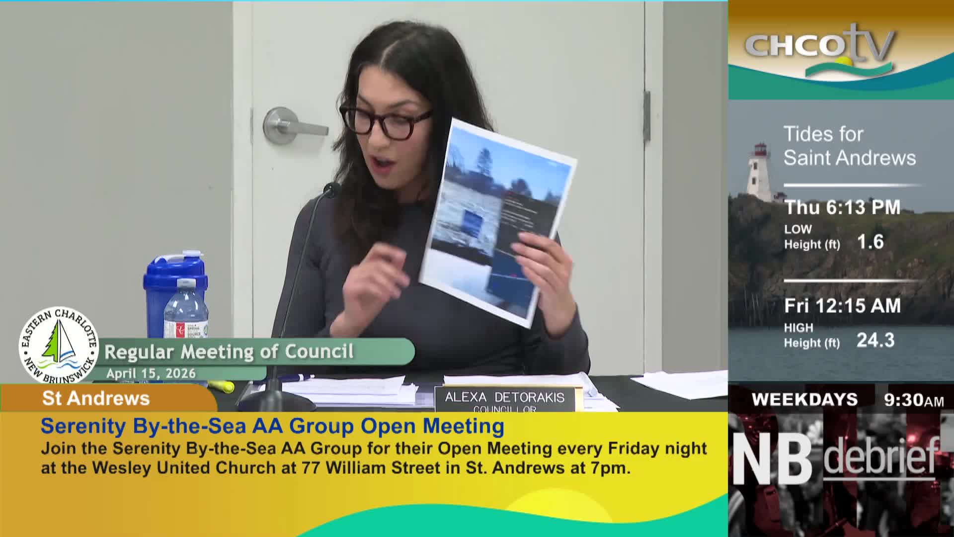 A woman in glasses holds up a document, speaking at a meeting in St. Andrews, New Brunswick. On the side, CHCO-TV displays tidal information for Saint Andrews and a news program.