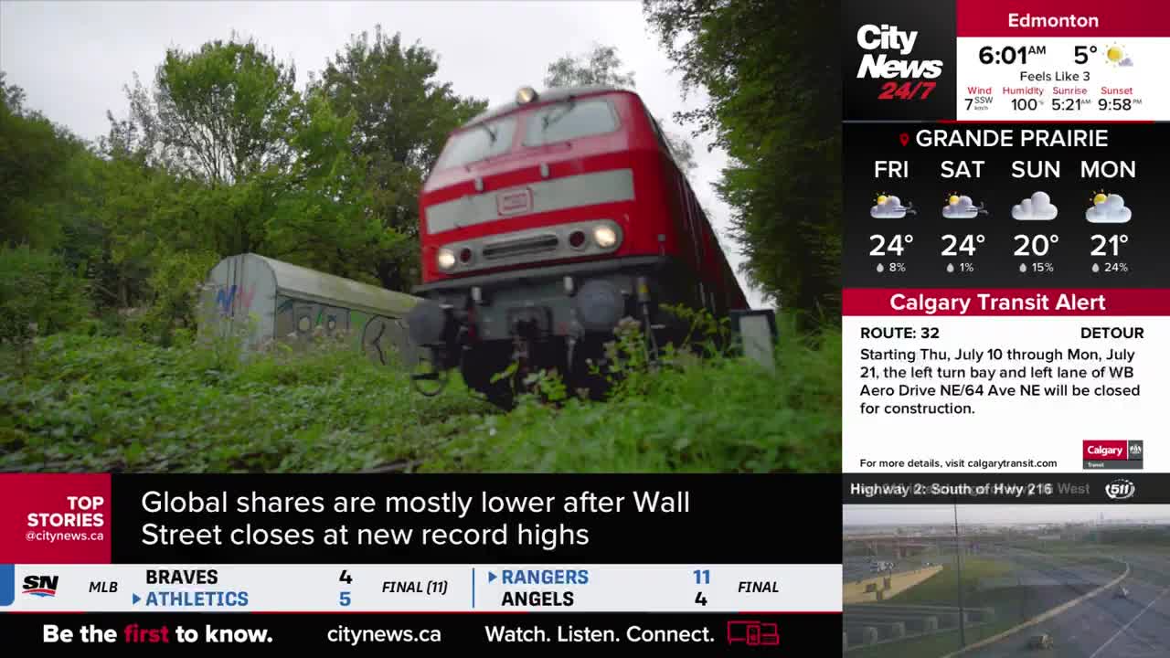 A red train engine, its headlights on, rolls toward me, framed by lush greenery. The CityNews Calgary screen shows a transit alert, and the train seems to be moving along a track in the city.
