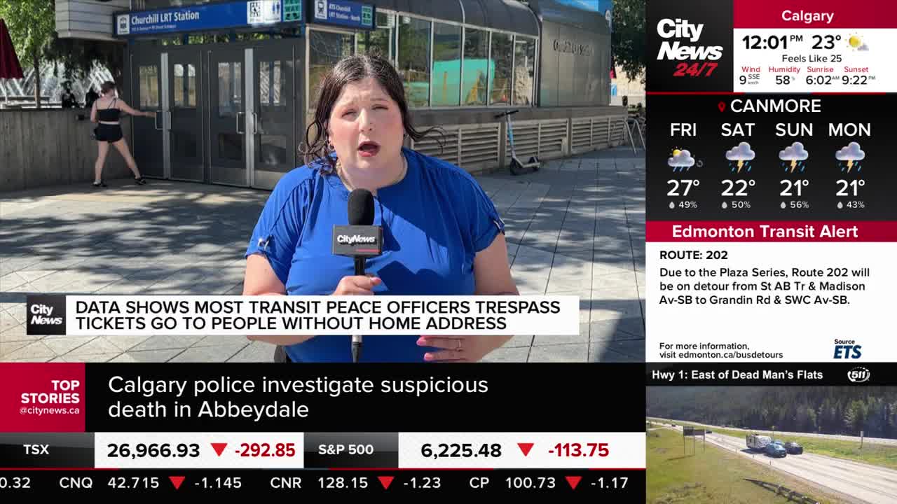 A CityNews Calgary reporter stands outside a transit station, speaking into a microphone. A woman in a black outfit walks toward the station entrance in the background.
