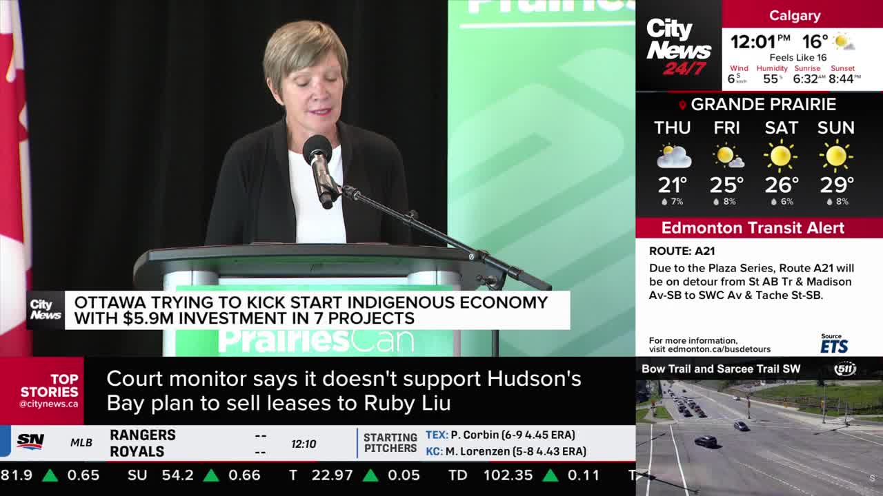 A woman in a black blazer stands behind a podium, speaking into a microphone. The CityNews Calgary logo and a graphic about an investment in the Indigenous economy are visible on the screen behind her.
