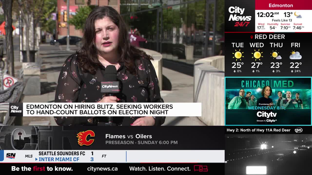 A CityNews reporter in Edmonton is speaking into a microphone, reporting on the city's need for election night workers. Behind her, the sidewalk and a stone wall are visible.
