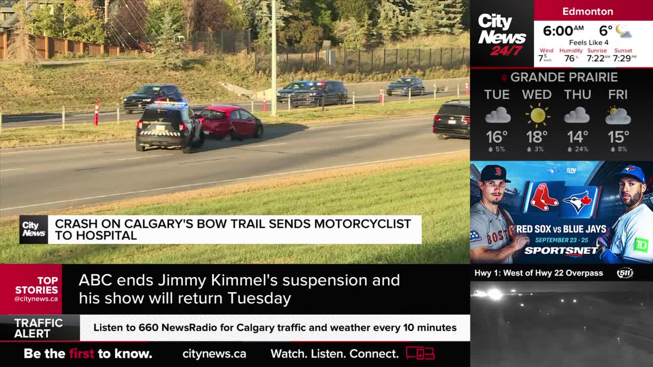A red car and a police vehicle are stopped on the Bow Trail in Calgary, near a grassy median.  CityNews Calgary reports a motorcyclist was sent to the hospital after a crash.

