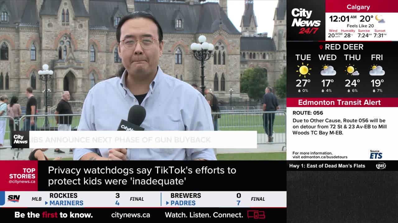 A CityNews Calgary reporter stands in front of a stone building, speaking into a microphone. Behind him, people stroll on the lawn as the news ticker scrolls across the bottom of the screen.
