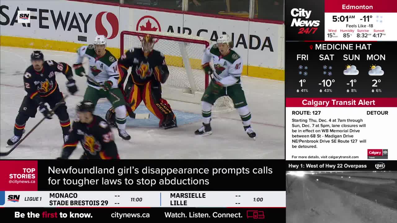 The goalie, in black and red, is crouched in front of the net, watching the puck. Players in green and black jerseys are skating around the net, ready to react.
The goalie, in black and red, is crouched in front of the net, watching the puck. Players in green and black jerseys are skating around the net, ready to react.