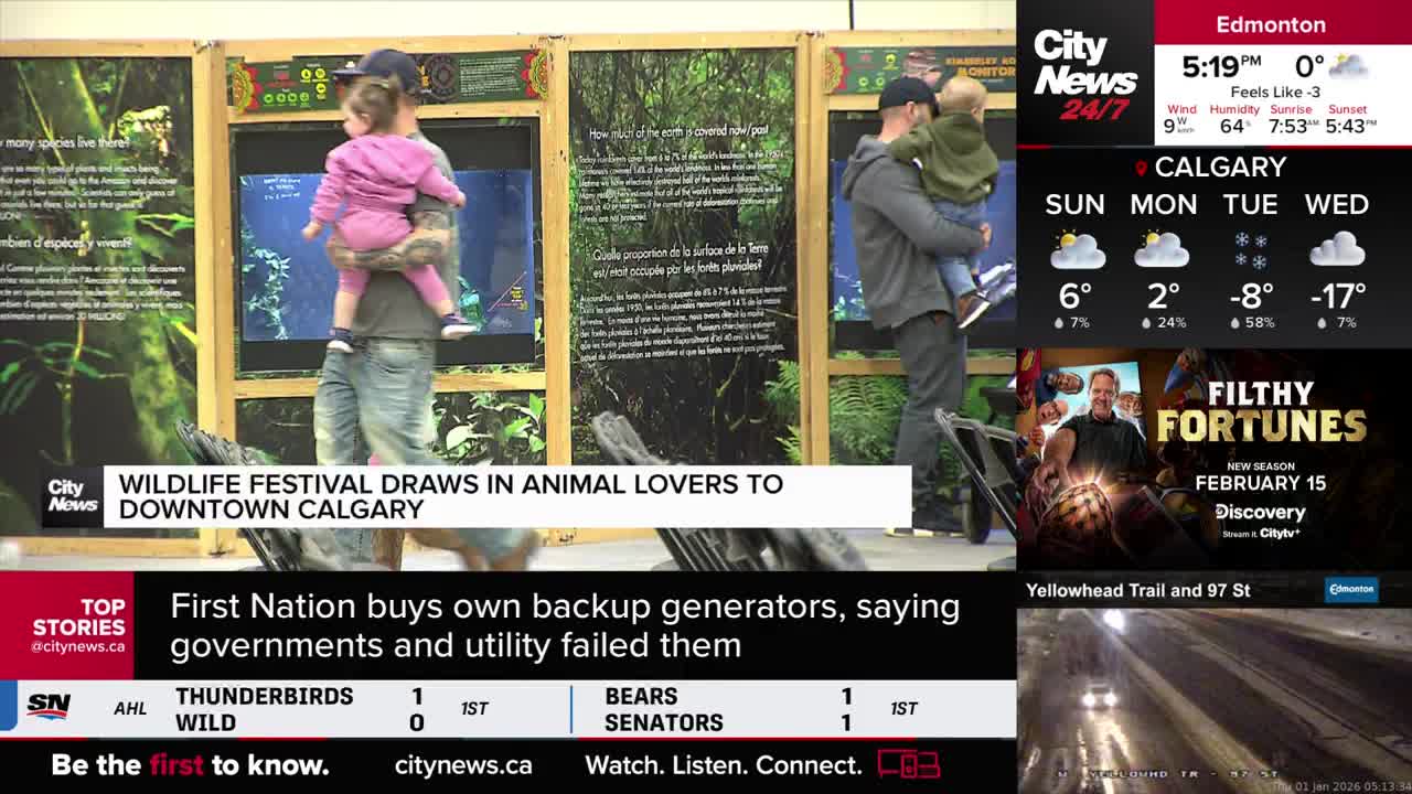 A man carries a child in a pink jacket, walking past an exhibit. Another man holds a child, looking towards the same display.