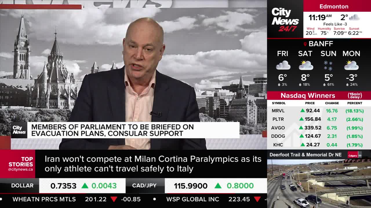 Cars are moving along a highway overpass. A news anchor is speaking in front of a backdrop of Parliament buildings.