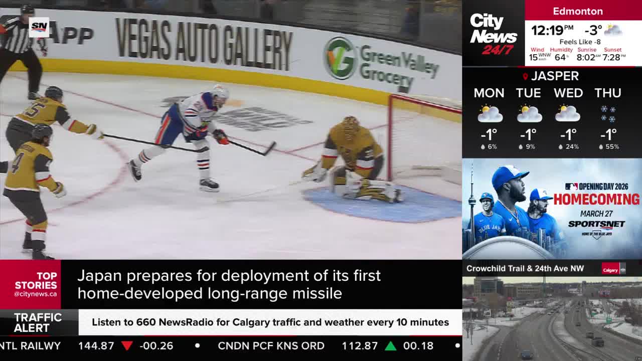 A hockey player in an orange and blue jersey skates towards the net, stick in hand. The goalie, in gold, is down on the ice, ready to make a save.