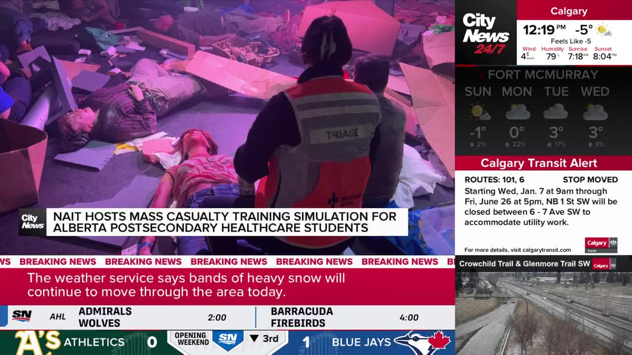 A person wearing a "Triage" vest kneels beside a simulated casualty on the floor. Around them, other individuals lie on the ground amidst scattered supplies, suggesting a training exercise for Alberta healthcare students.