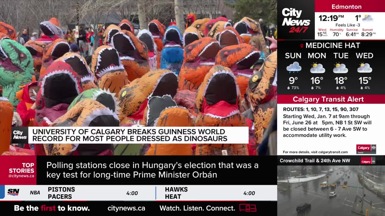 A crowd of people in inflatable dinosaur costumes fills the frame, their heads bobbing. This is the University of Calgary breaking a Guinness World Record.