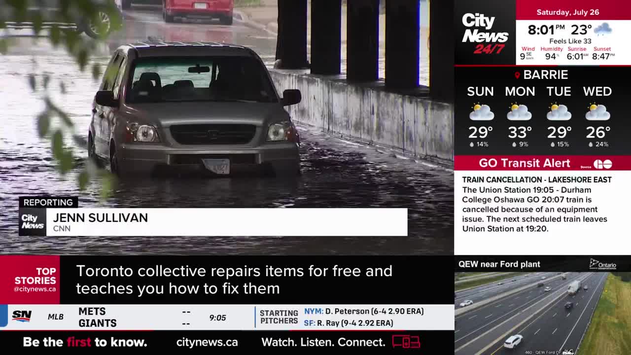 A silver SUV slowly navigates a flooded street under a bridge, captured on CityNews Toronto. The water is high enough to reach the vehicle's tires.

