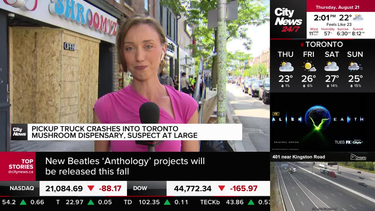 A reporter from CityNews Toronto stands in front of a dispensary, its storefront boarded up with plywood. Behind her, a line of cars sits parked on a Toronto street.
