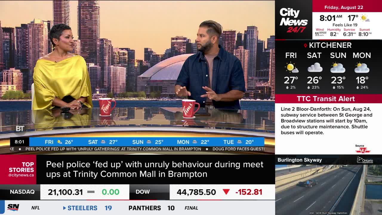 Two people sit at a desk, discussing something on CityNews Toronto. A red Tim Hortons mug sits between them, while a weather report for Kitchener and a TTC transit alert flash on the right.

