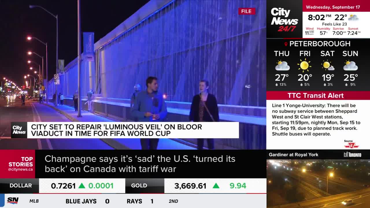 Two people stand on a sidewalk, facing a wall that appears to be a water feature, illuminated with blue light. The CityNews Toronto logo and a headline about the Bloor Viaduct are visible in the foreground.
