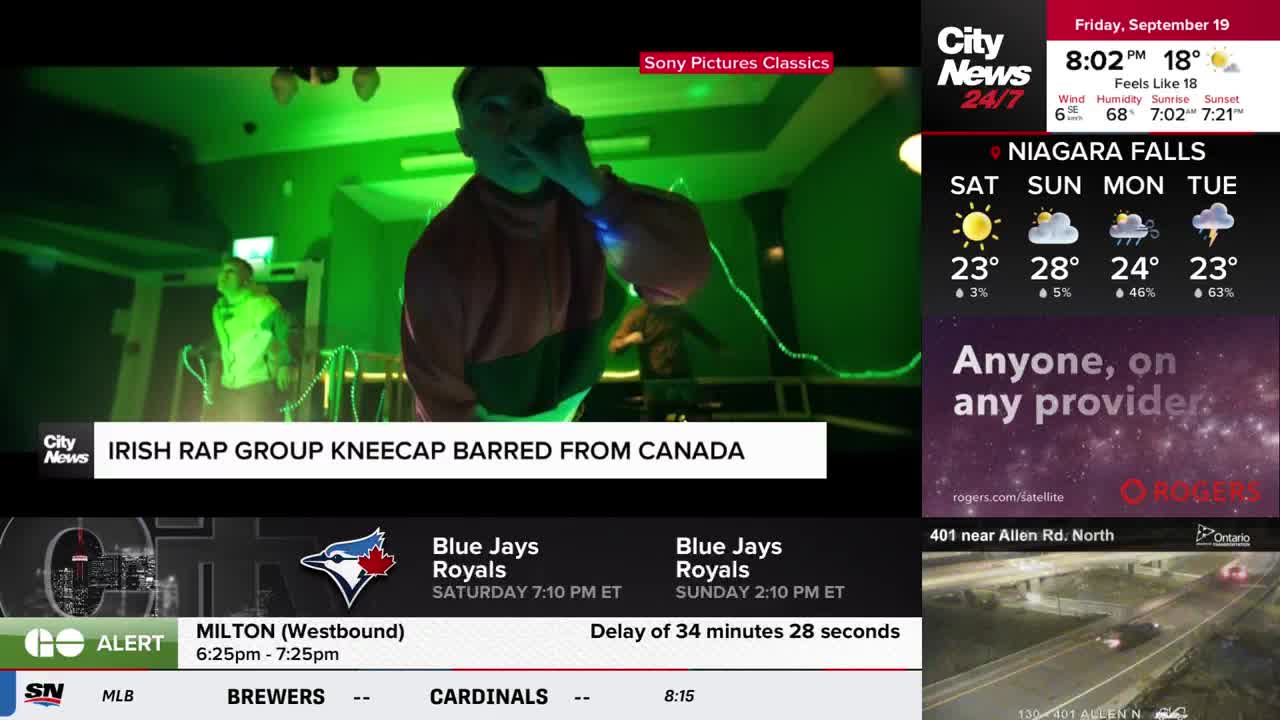A man in a red and pink top sings into a microphone, lit by green lights, as CityNews Toronto reports on the Irish rap group Kneecap being barred from Canada. The weather report for Niagara Falls is displayed on the right side of the screen.
