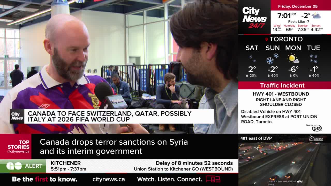 A bald man in a purple and white shirt speaks into a microphone held by someone off-camera, with a CityNews Toronto graphic displayed below. Behind them, people sit and stand, and the news ticker scrolls across the bottom.
