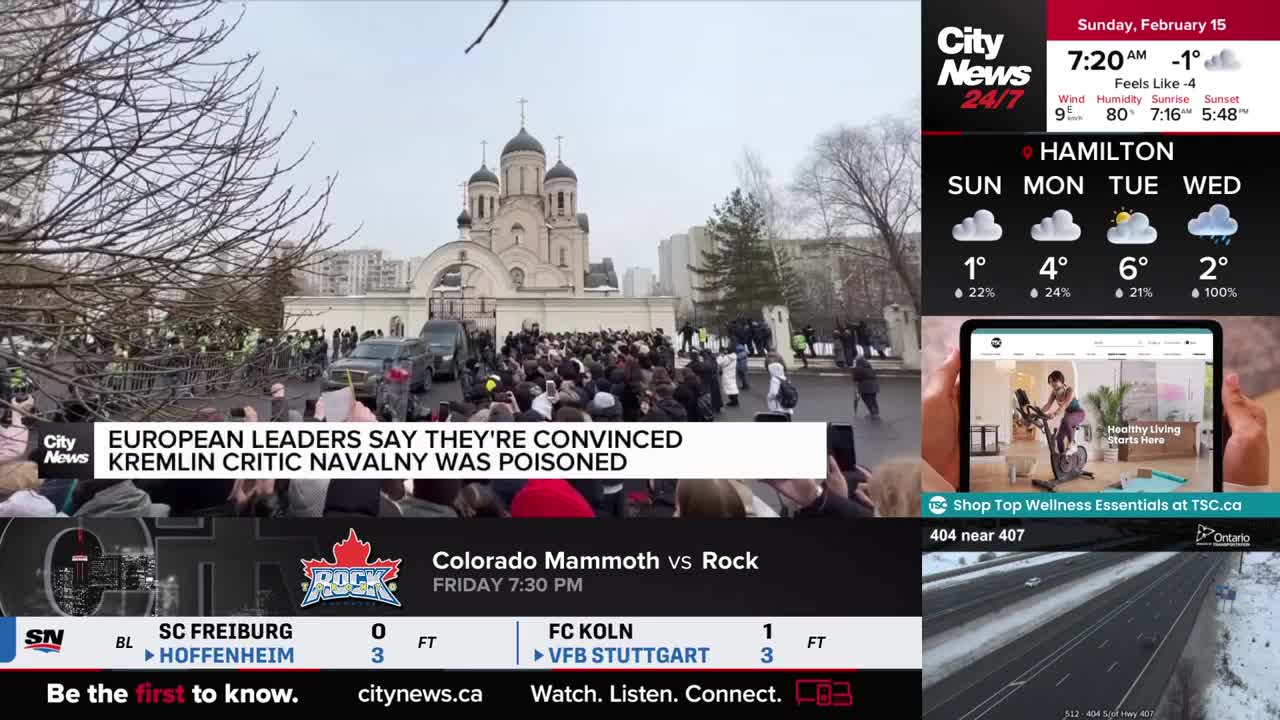 A large crowd has gathered outside a grand, domed building. Several black cars are parked near the entrance, and people are holding up phones to record.