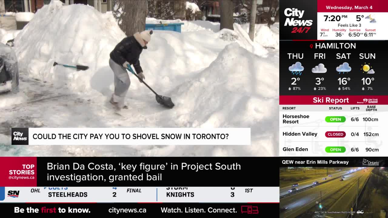 A person is shoveling a large pile of snow in front of a house. Another shovel lies discarded in the snow nearby.