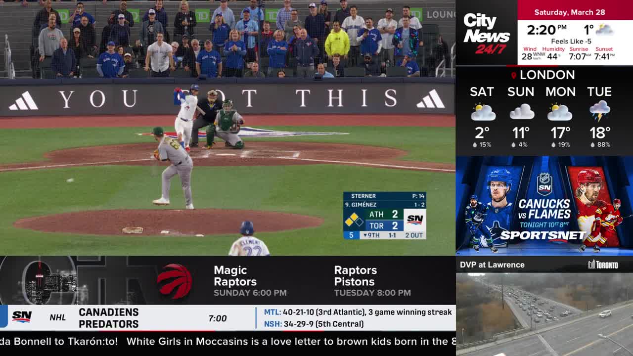 A pitcher in a grey uniform winds up, releasing the ball toward home plate. The batter, in white, swings, while the catcher crouches behind him.