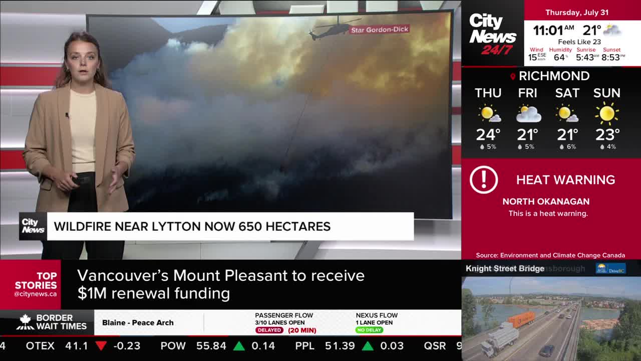 A CityNews Vancouver anchor stands in front of a screen showing a wildfire near Lytton, with a helicopter visible in the smoke. The screen also displays a heat warning for North Okanagan.
