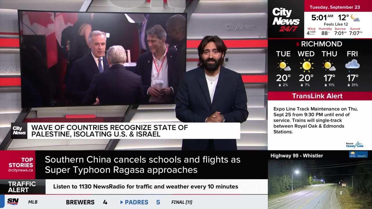 A CityNews Vancouver anchor stands in front of a screen showing a news report. The screen displays a still image of several men in suits, with the Canadian flag visible.
