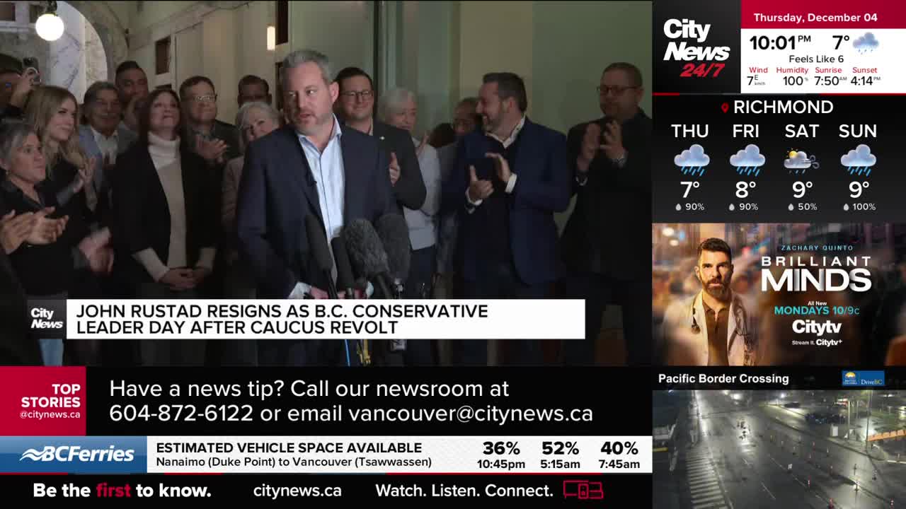 John Rustad, surrounded by a crowd, stands before microphones, speaking to the press. Behind him, people clap and watch as the CityNews Vancouver headline announces his resignation as B.C. Conservative leader.
