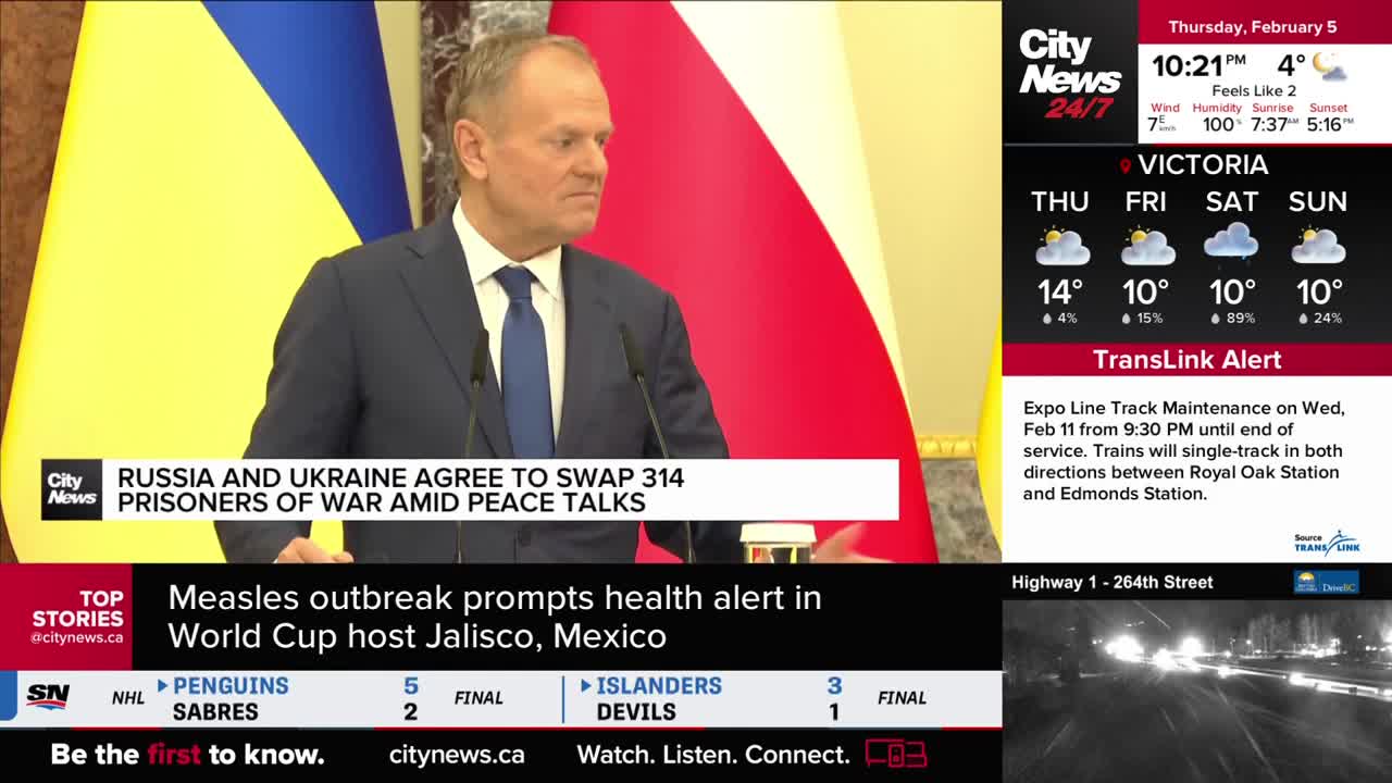 A man in a dark suit stands at a podium, speaking in front of Ukrainian and Polish flags. On the screen, CityNews Vancouver reports that Russia and Ukraine have agreed to a prisoner swap.