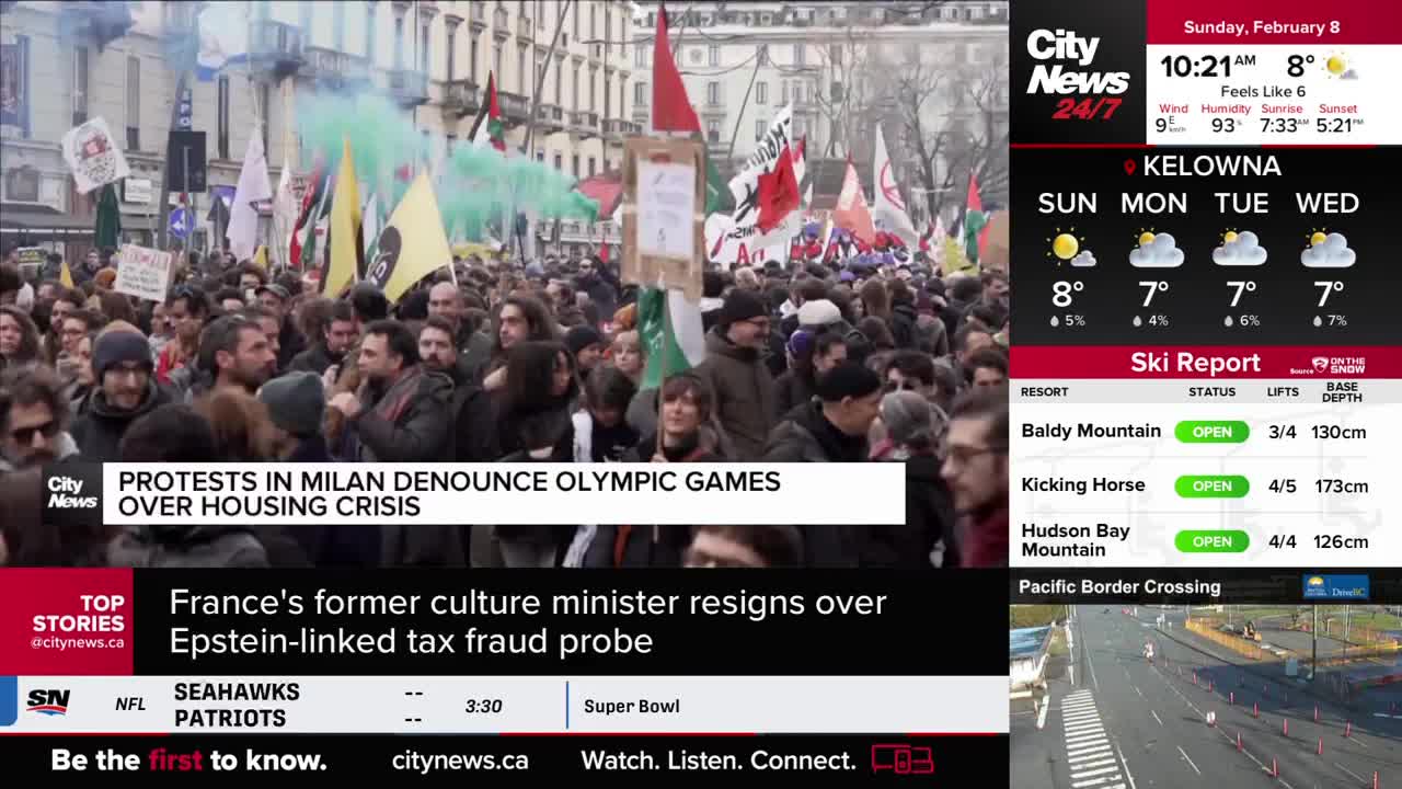 A crowd marches, holding flags and signs, with green smoke billowing into the air. CityNews Vancouver reports on protests in Milan denouncing the Olympic Games over a housing crisis.