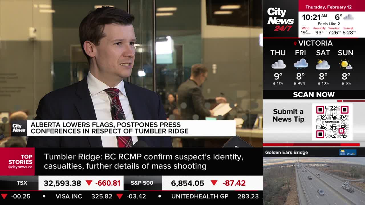 A man in a suit and tie speaks into microphones, his expression serious. Behind him, another person is visible, sorting through papers. A man in a suit and tie speaks into microphones, his expression serious. Behind him, another person is visible, sorting through papers.