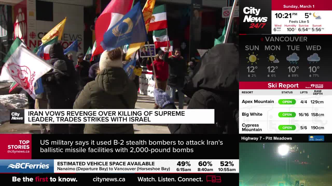 A crowd of people holds up many colourful flags, some with images of lions and suns. The CityNews Vancouver banner at the bottom of the screen mentions Iran vowing revenge. A crowd of people holds up many colourful flags, some with images of lions and suns. The CityNews Vancouver banner at the bottom of the screen mentions Iran vowing revenge.