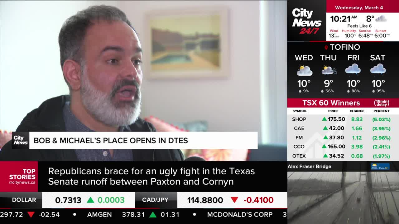 A man with a grey beard is speaking, his mouth open. A news ticker scrolls below, reporting on a political fight in Texas and stock market updates from Canada.