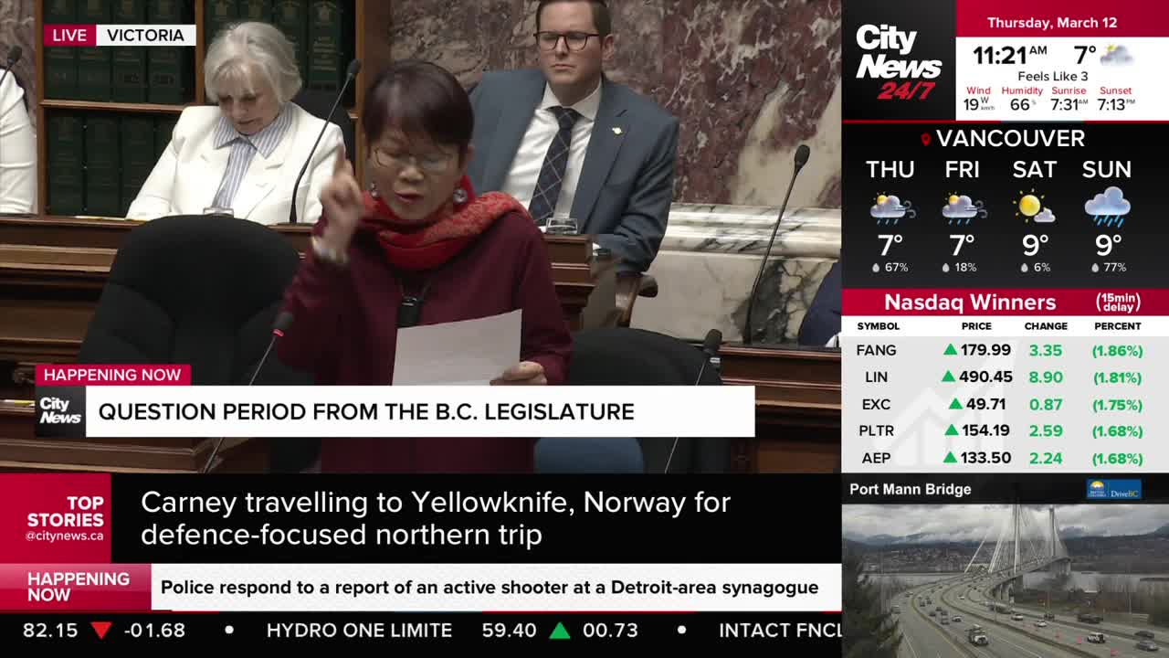 A woman in a maroon sweater and red scarf speaks animatedly, holding a piece of paper. She's at a podium in the B.C. Legislature during question period.
