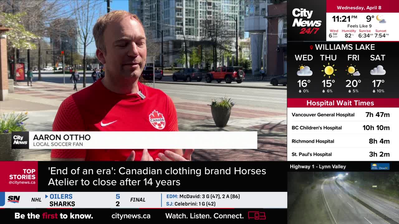 A man in a red Canadian soccer jersey speaks on a Vancouver street. Cars pass behind him on the road.