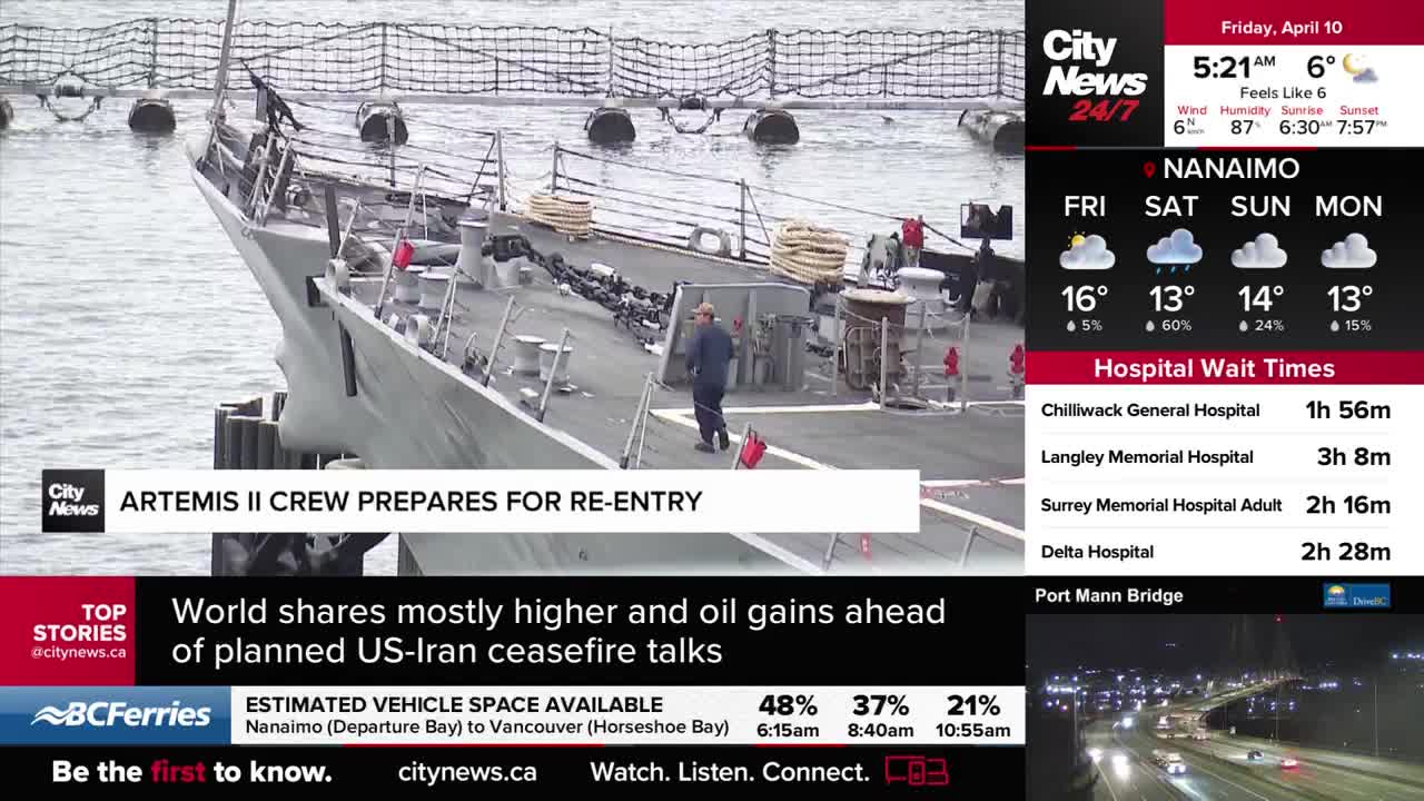 A lone figure in blue walks across the deck of a large grey ship docked in Vancouver. The ship's railing is lined with coiled ropes and metal cleats.