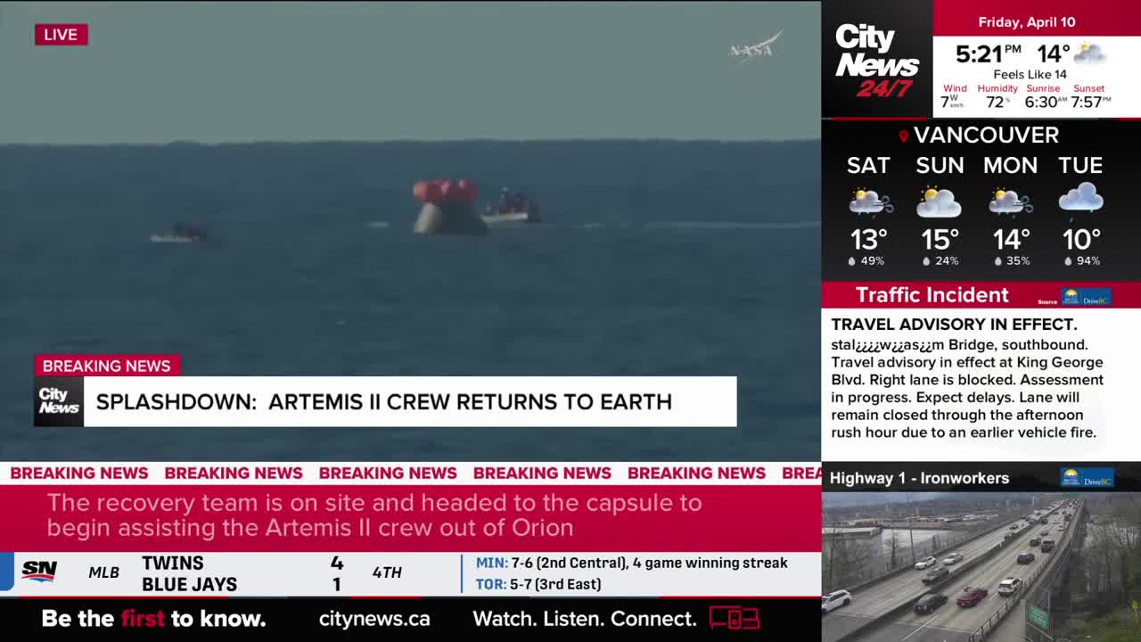 A recovery boat approaches a capsule bobbing in the ocean, its red parachutes still visible. Another smaller boat is already near the capsule, ready to assist the Artemis II crew.