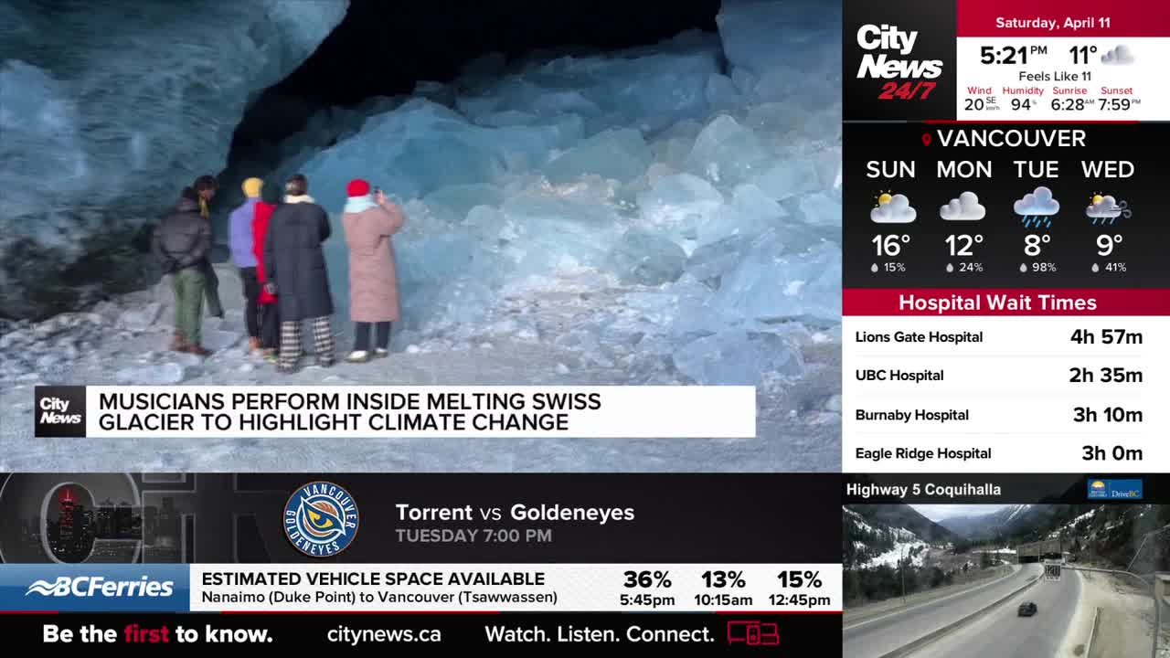 A group of people stand inside a cavern of ice, their backs to us. One person in a long coat and red hat raises a camera to capture the scene.
