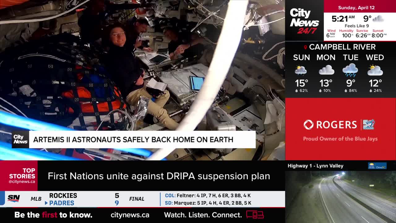 Astronauts are seated inside a spacecraft, surrounded by equipment and wires. A banner across the bottom of the screen announces "ARTEMIS II ASTRONAUTS SAFELY BACK HOME ON EARTH."