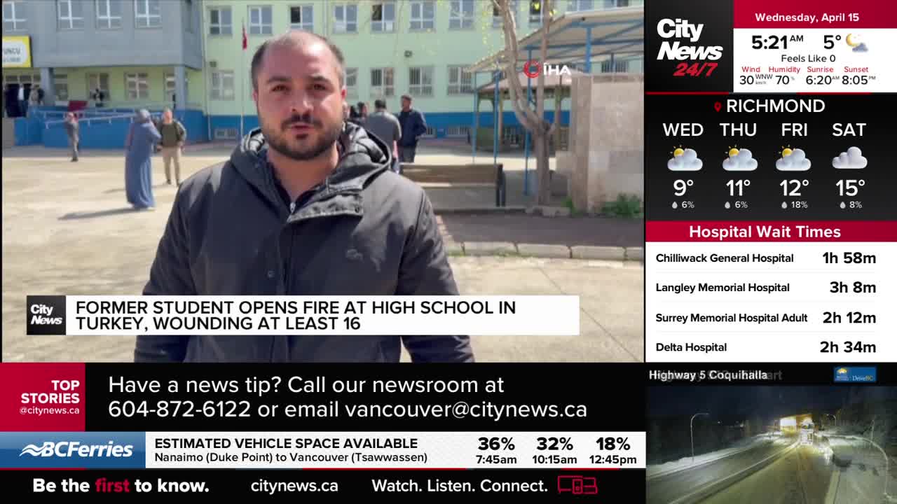 A man in a dark jacket stands in front of a school building, speaking to the camera. Behind him, several people walk across a paved courtyard. A man in a dark jacket stands in front of a school building, speaking to the camera. Behind him, several people walk across a paved courtyard.